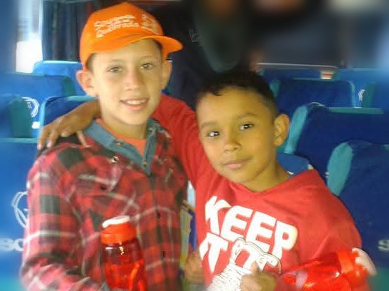 Camilo y Daniel de niños, abrazados y sonriendo en un bus escolar